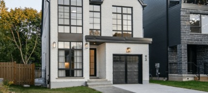 A photo of a home with a white exterior and large, black-framed windows, a black front door, and a black garage door.