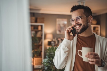 A man standing by the window with a cup of coffee in his home.