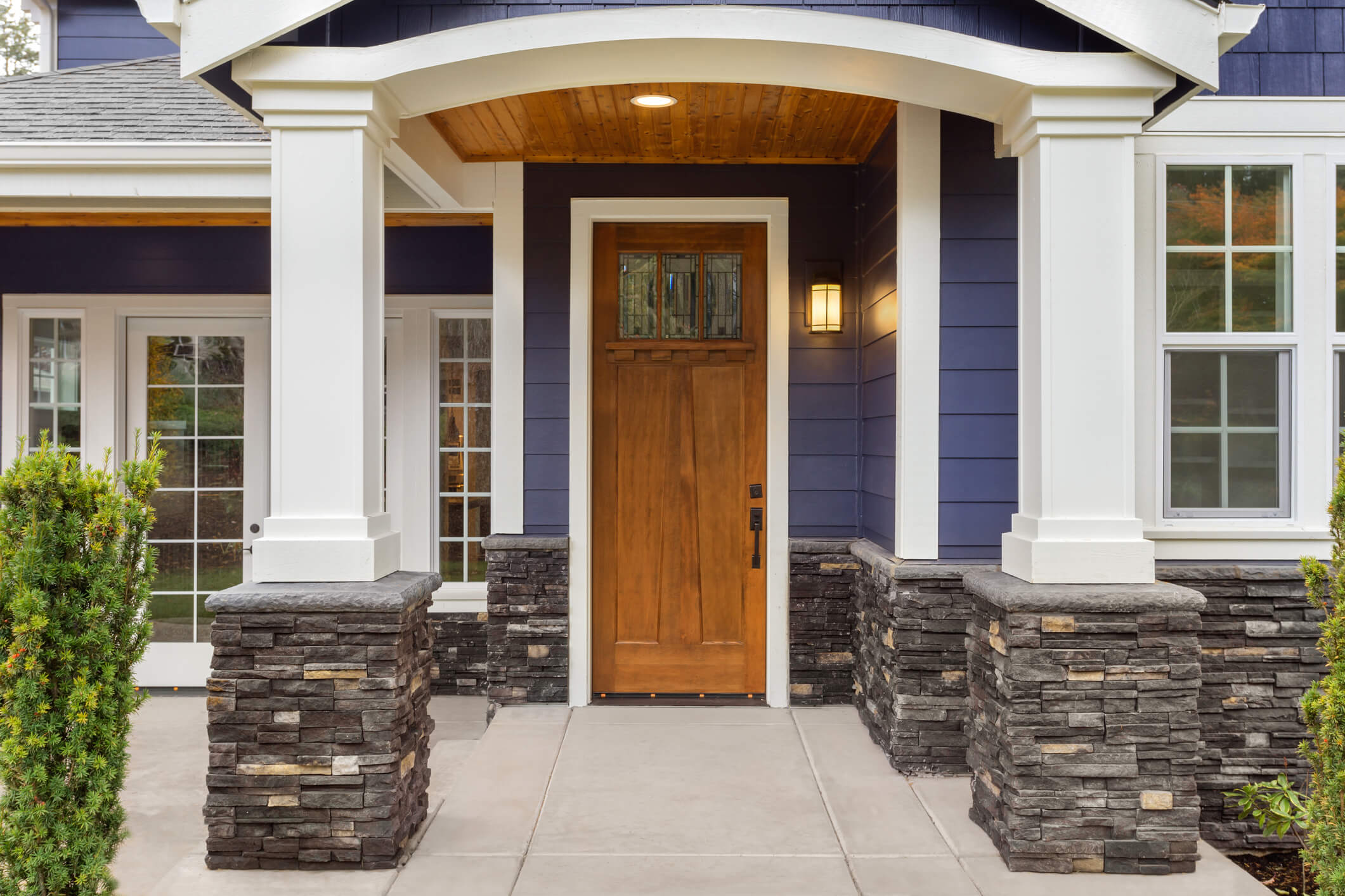 Wooden front door with glass panels on blue craftsman home with stone pillars