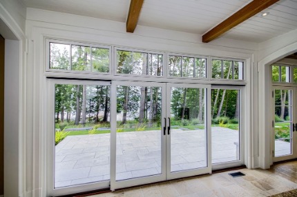White lift-and-slide patio door with transom windows looking out to wooded backyard