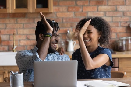A photo of two people sitting a table next to a laptop, about to give each other a high five.
