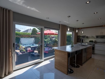 A photo of a lift and slide door in a kitchen, leading out to a deck with a hot tub and patio furniture. 