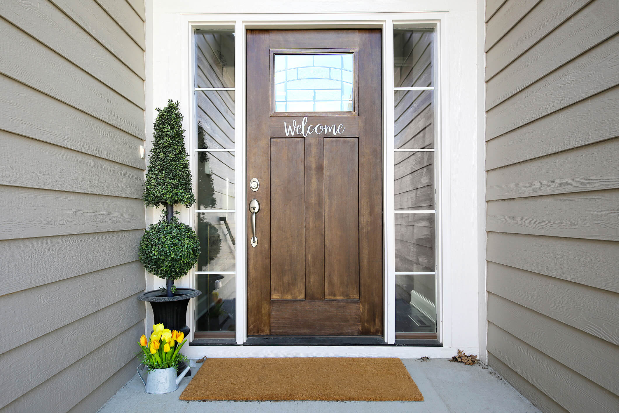 Wood front door with small glass window, Welcome sign, sidelights, and spring tulips