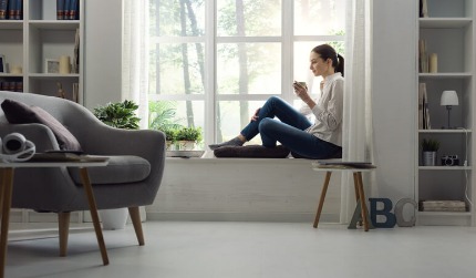 A young woman relaxing at home next to a window and having a cup of coffee.