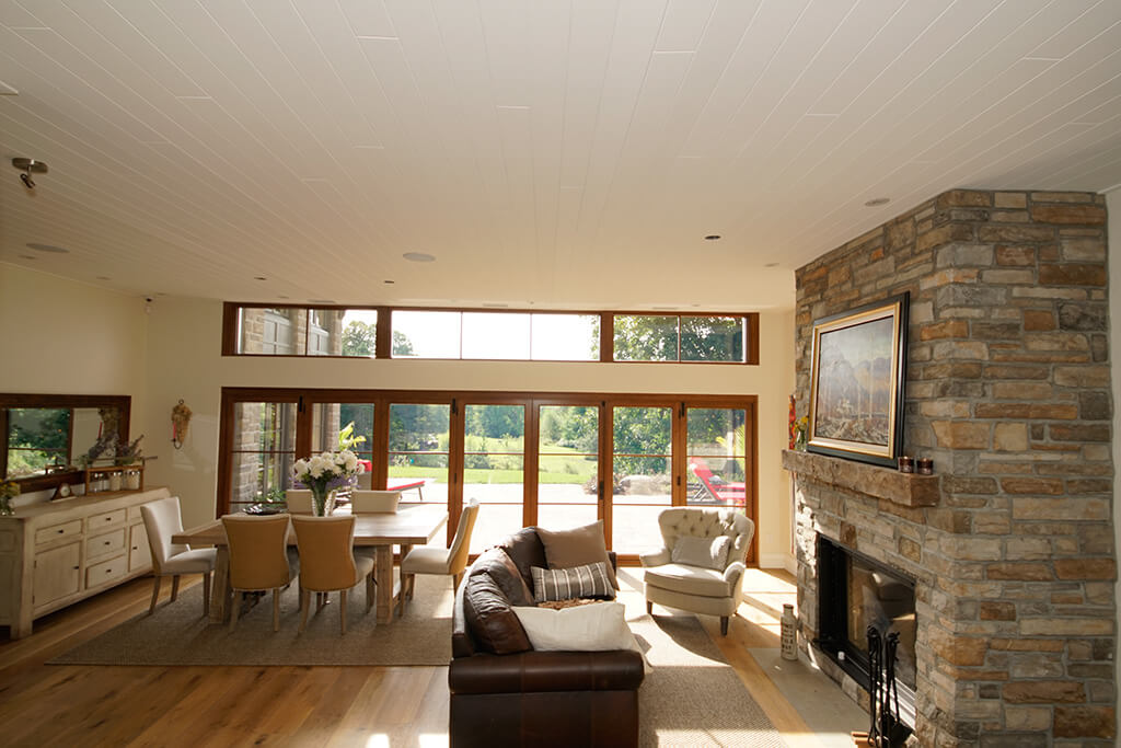 Open-concept living and dining room with wooden bi-fold patio doors open to backyard with stone fireplace