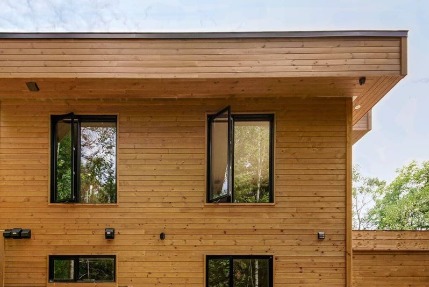 A photo of open windows with black frames installed in a two-story house with a wooden exterior.